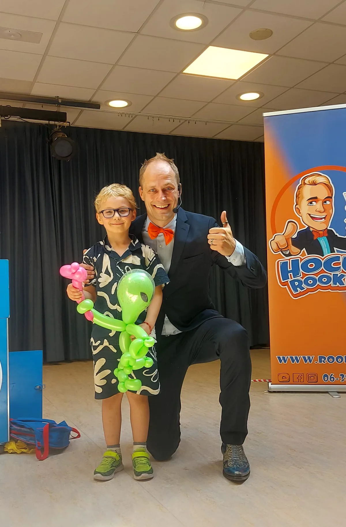 Kindergoochelaar Hocus Rookus met jonge vrijwilliger en ballonfiguren na de show — duim omhoog