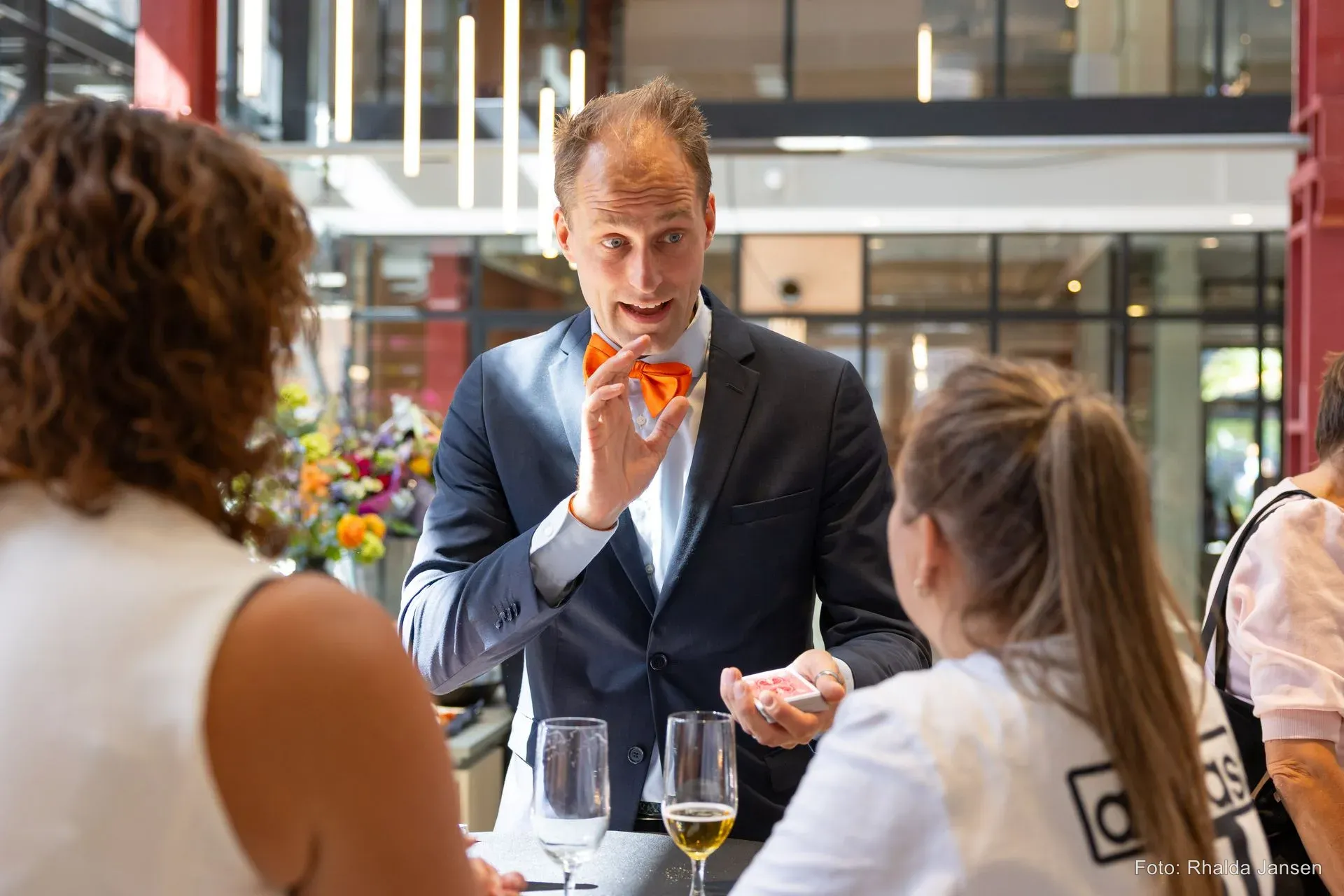 Goochelaar Teun Rookus met oranje vlinderstrik toont een kaarttruc voor gasten op een zakelijk event