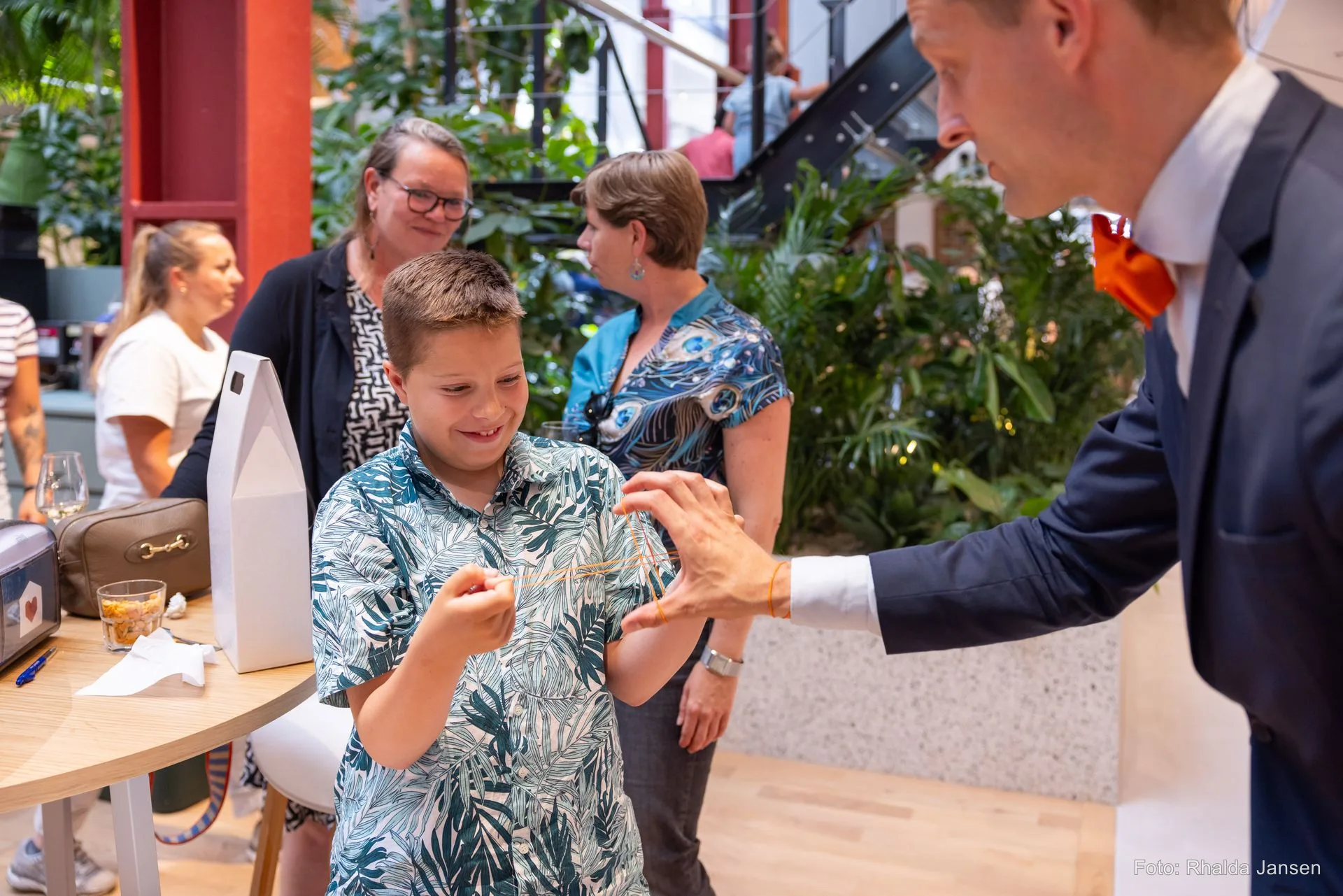 Kind kijkt glimlachend vol verwondering naar de handen van tafelgoochelaar Teun Rookus — volwassenen kijken mee tijdens een event